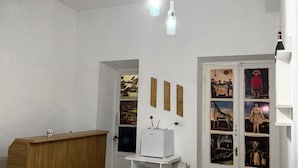 Un salón moderno con un mostrador de recepción de madera, una mesa blanca y un armario blanco. Hay dos lámparas colgantes y una puerta decorada con una obra de arte.