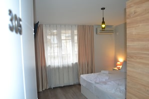 A hotel room with a bed, a nightstand with a lamp, a window with curtains, and an air conditioning unit. - Rustaveli 36 Hotel (Tbilisi)