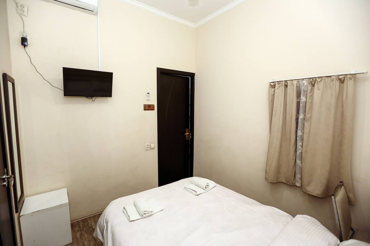 A hotel room with a bed, a TV mounted on the wall, a door, and a window with curtains.