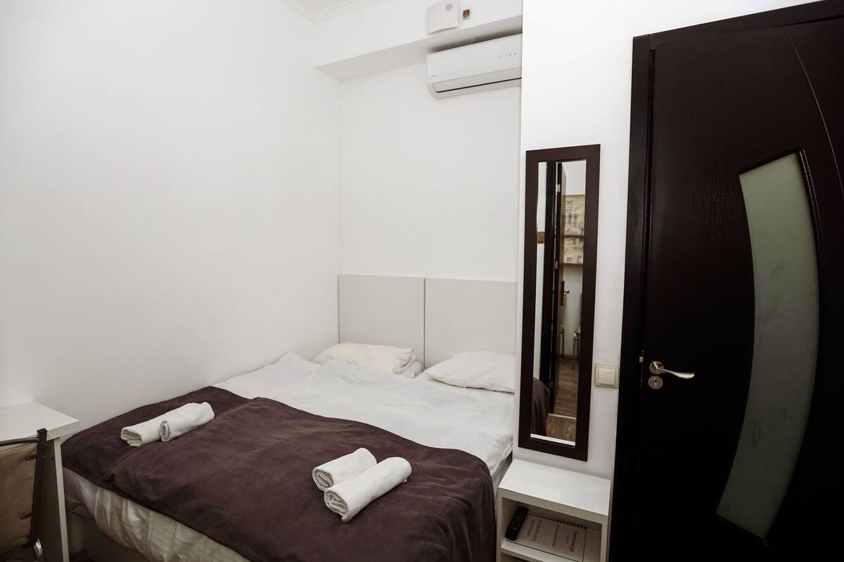 A hotel room with a bed, a nightstand, a mirror, and a door.