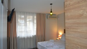 Una habitación de hotel con cama, aire acondicionado, lámpara de noche y ventana con cortinas.