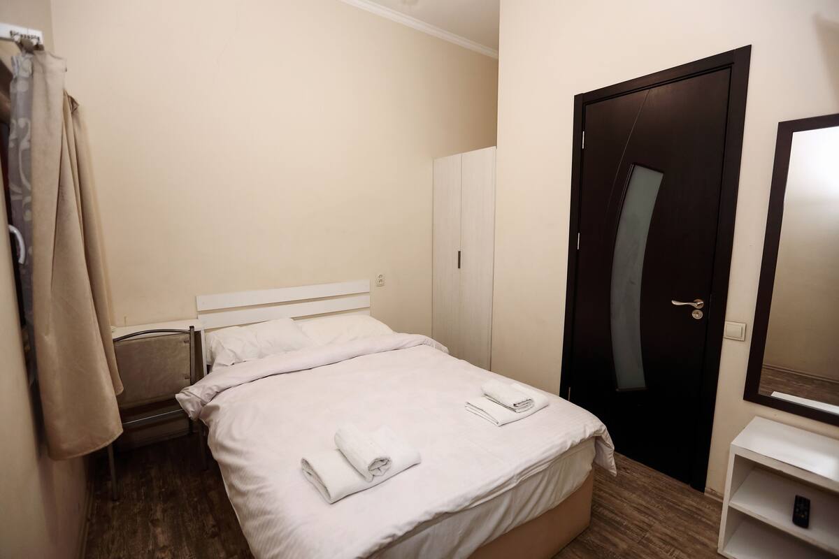 A hotel room with a bed, a wardrobe, a mirror, and a shelf with a remote control.