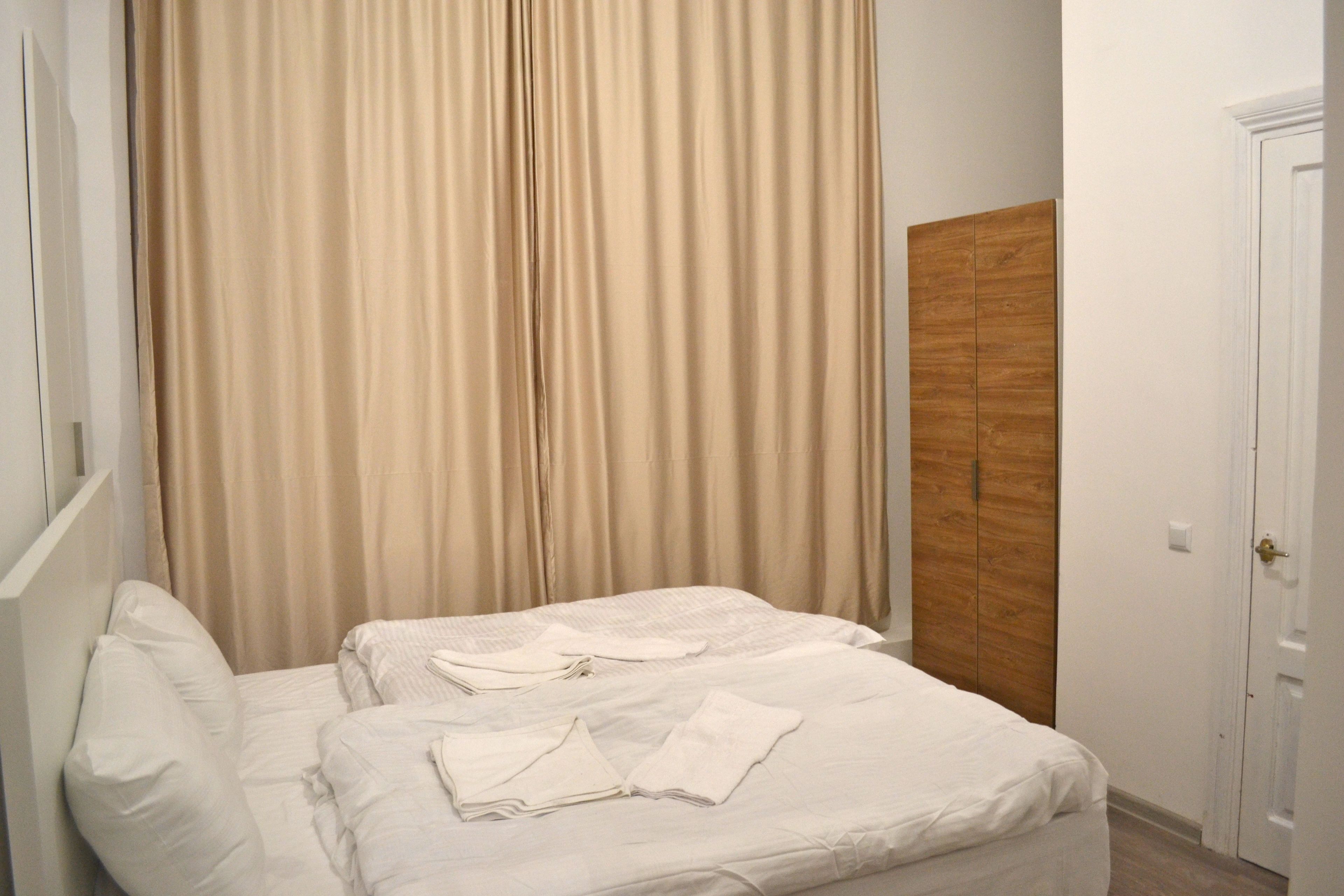 Uma cama bem arrumada com roupa de cama e toalhas brancas, um guarda-roupa de madeira e uma porta branca.