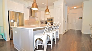 A modern kitchen with white cabinetry, stainless steel appliances, and a central island with bar stools.