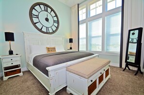 A bedroom with a large wall clock, a bed with a headboard, bedside tables with lamps, a bench, and a full-length mirror. - Time to Chill 3 Bedroom Condo By Coastal Dreamin (Santa Rosa Beach)