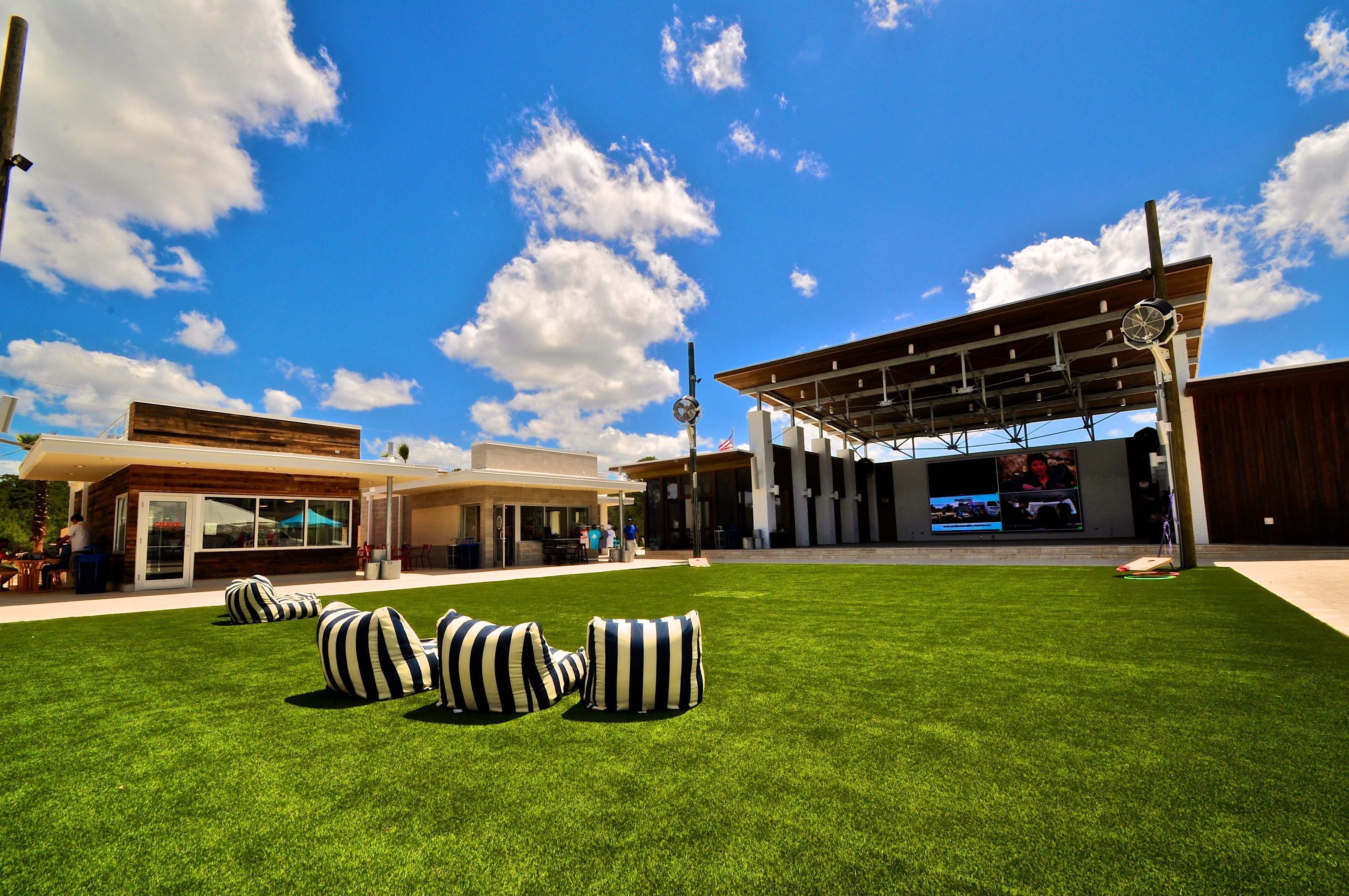A modern outdoor area with a grassy lawn, striped bean bags, and a covered seating area with a large screen.
