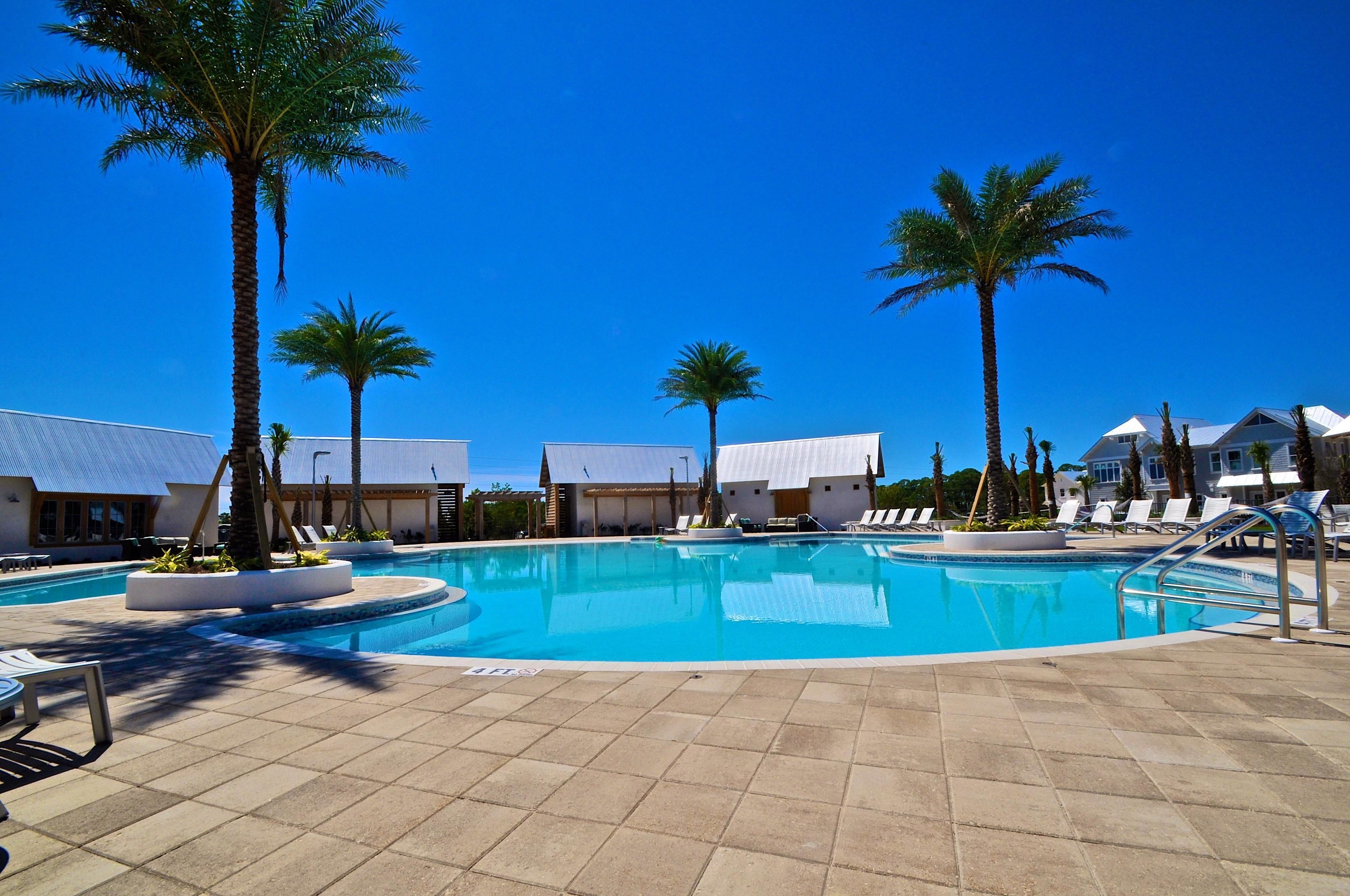 Una piscina con palmeras, sillas de descanso y un cielo azul despejado.