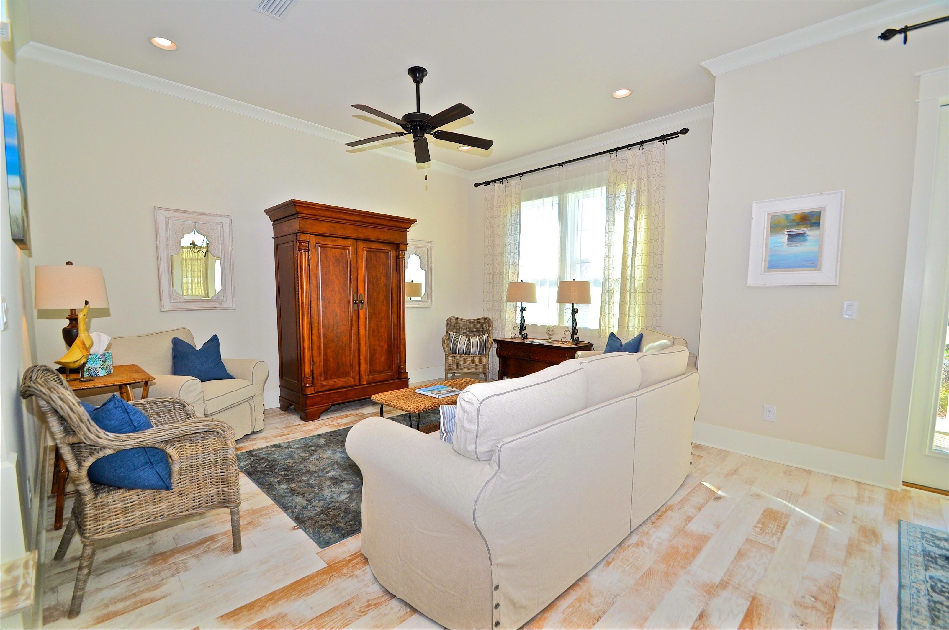 A living room with a ceiling fan, a large wooden cabinet, a beige sofa, a wicker chair, and a small table with a lamp.