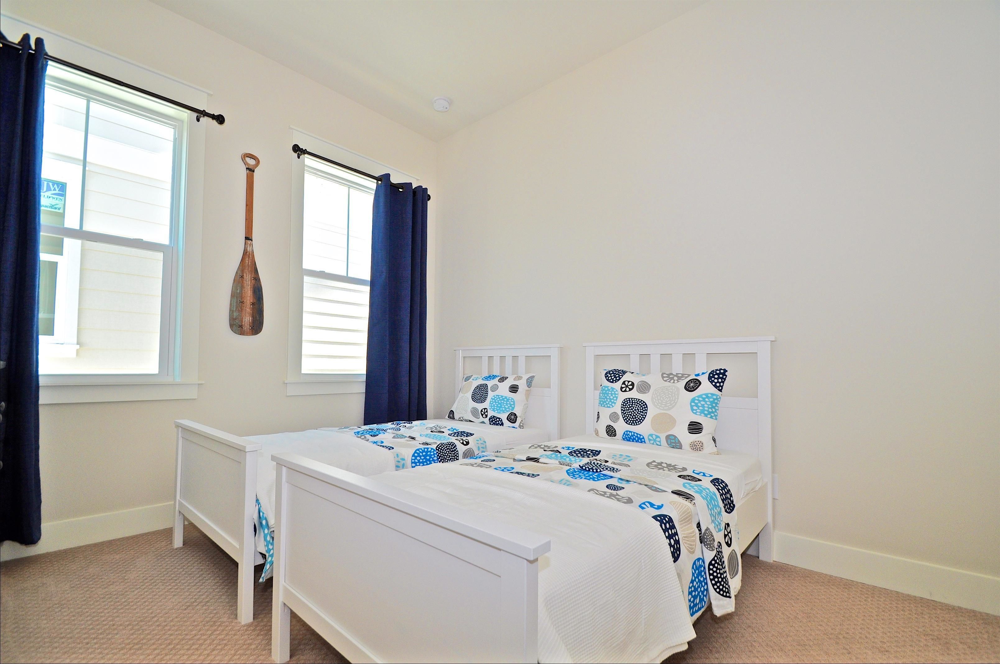 A bedroom with two single beds, a window with curtains, and a bat hanging on the wall.