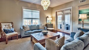 A living room with a grey sofa, a wooden coffee table, a wicker chair, and a chandelier. - Redfish Village M2 417 3 Bedroom Condo By Coastal Dreamin (Santa Rosa Beach)