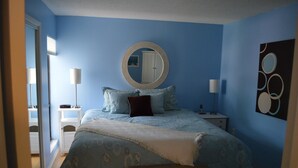 A bedroom with a bed, bedside tables, a mirror, and a wall art piece. - Cove II 822F 2 Bedroom Condo By Midnight Cove II (Siesta Key)