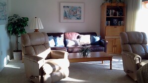 A living room with a brown leather sofa, two leather armchairs, a wooden coffee table, a potted plant, a lamp, and a bookshelf. - Cove II 833F 2 Bedroom Condo By Midnight Cove II (Siesta Key)