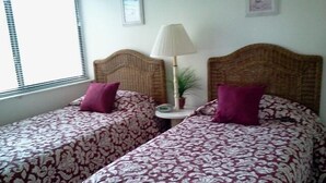 Two twin beds with patterned bedding, a bedside lamp, and a small table with a plant. - Cove II 833F 2 Bedroom Condo By Midnight Cove II (Siesta Key)