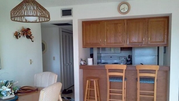 A compact kitchen with wooden cabinets, a sink, and two bar stools. - Cove II 833F 2 Bedroom Condo By Midnight Cove II (Siesta Key)