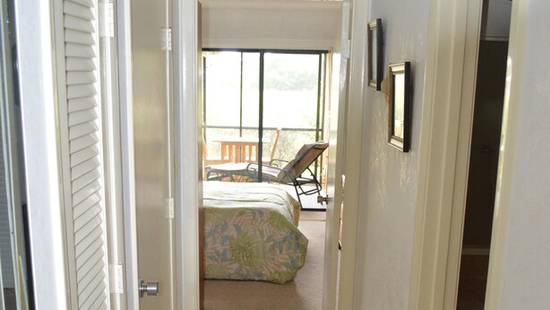 A narrow hallway with a bed in the background, a bench, and a door on the right. - Cove II 912C 2 Bedroom Condo By Midnight Cove II (Siesta Key)