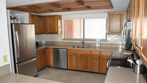 A kitchen with wooden cabinets, stainless steel appliances, a dishwasher, and a window with blinds. - Cove II 912C 2 Bedroom Condo By Midnight Cove II (Siesta Key)