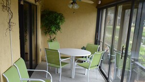 A covered patio area with a table and chairs, a cushioned bench, and a ceiling fan. - Cove II 912C 2 Bedroom Condo By Midnight Cove II (Siesta Key)