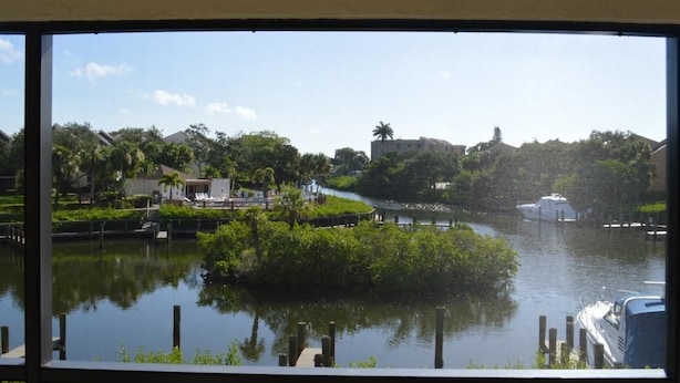 A river with a boat docked on the right, surrounded by greenery and buildings in the background. - Cove II 922C 2 Bedroom Condo By Midnight Cove II (Siesta Key)