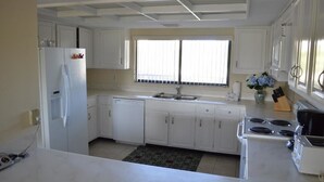 A kitchen with white cabinets, a refrigerator, a stove, and a window with blinds. - Cove II 922C 2 Bedroom Condo By Midnight Cove II (Siesta Key)