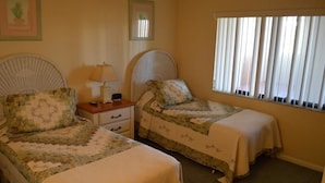 A bedroom with two single beds, a nightstand, a lamp, and a window with blinds. - Cove II 922C 2 Bedroom Condo By Midnight Cove II (Siesta Key)