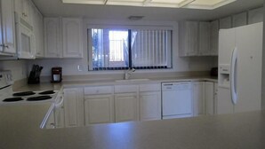 A kitchen with white cabinets, a window with blinds, a stove, and a refrigerator.
