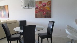 A dining area with a round table, four chairs, a modern chandelier, and two pieces of wall art.