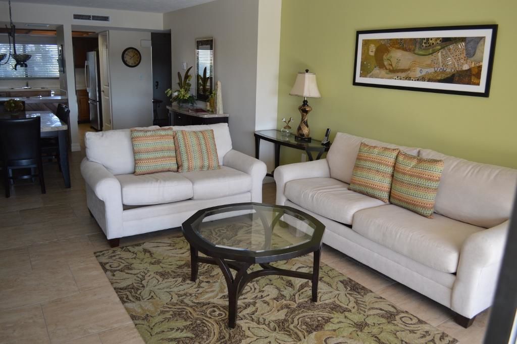 A living room with two white sofas, a glass coffee table, and a patterned rug.