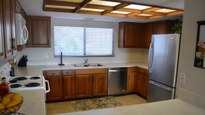 Una cocina con armarios de madera, un refrigerador de acero inoxidable, horno empotrado y una ventana con persianas.