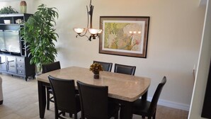 Un comedor con una mesa rectangular, seis sillas, un florero con flores, una lámpara de pared y un cuadro enmarcado.