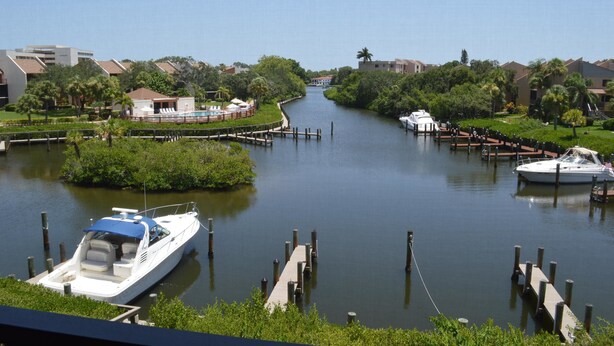 A canal with boats docked, surrounded by greenery and buildings. - Cove II 934C 2 Bedroom Condo By Midnight Cove II (Siesta Key)