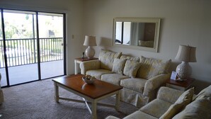 A living room with a sofa set, a coffee table, two lamps, and a large window with a view of the outside. - Cove II 934C 2 Bedroom Condo By Midnight Cove II (Siesta Key)
