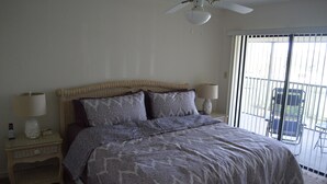 A bedroom with a bed, two bedside tables with lamps, a ceiling fan, and a view through a sliding glass door. - Cove II 934C 2 Bedroom Condo By Midnight Cove II (Siesta Key)