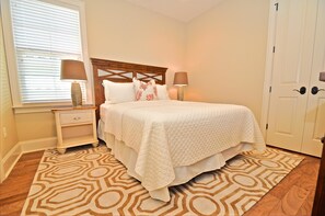 A neatly made bed with a quilted white cover, two bedside lamps, a nightstand with a drawer, and a patterned rug on a wooden floor. - Sandestin Vacation Rental by Coastal Dreamin (Miramar Beach)