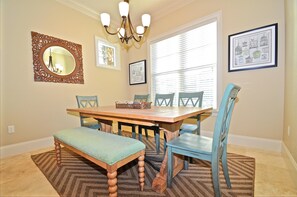 A dining room with a wooden table, blue chairs, a bench, a chandelier, and framed artwork on the walls. - Sandestin Vacation Rental by Coastal Dreamin (Miramar Beach)