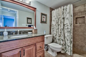 A bathroom with a granite countertop, a white toilet, a shower curtain with a bamboo pattern, and two framed pictures on the wall. - 221 Audubon 3 Bedroom Holiday Home By Coastal Dreamin (Miramar Beach)