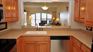 A kitchen with wooden cabinets, a stainless steel dishwasher, and a large mirror reflecting a dining area with a table and chairs.