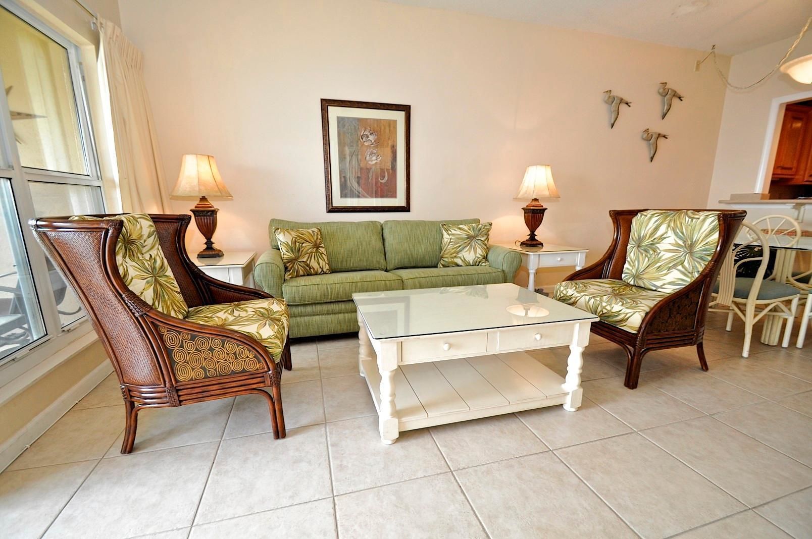 A living room with a green sofa, two armchairs, a glass coffee table, and two lamps.