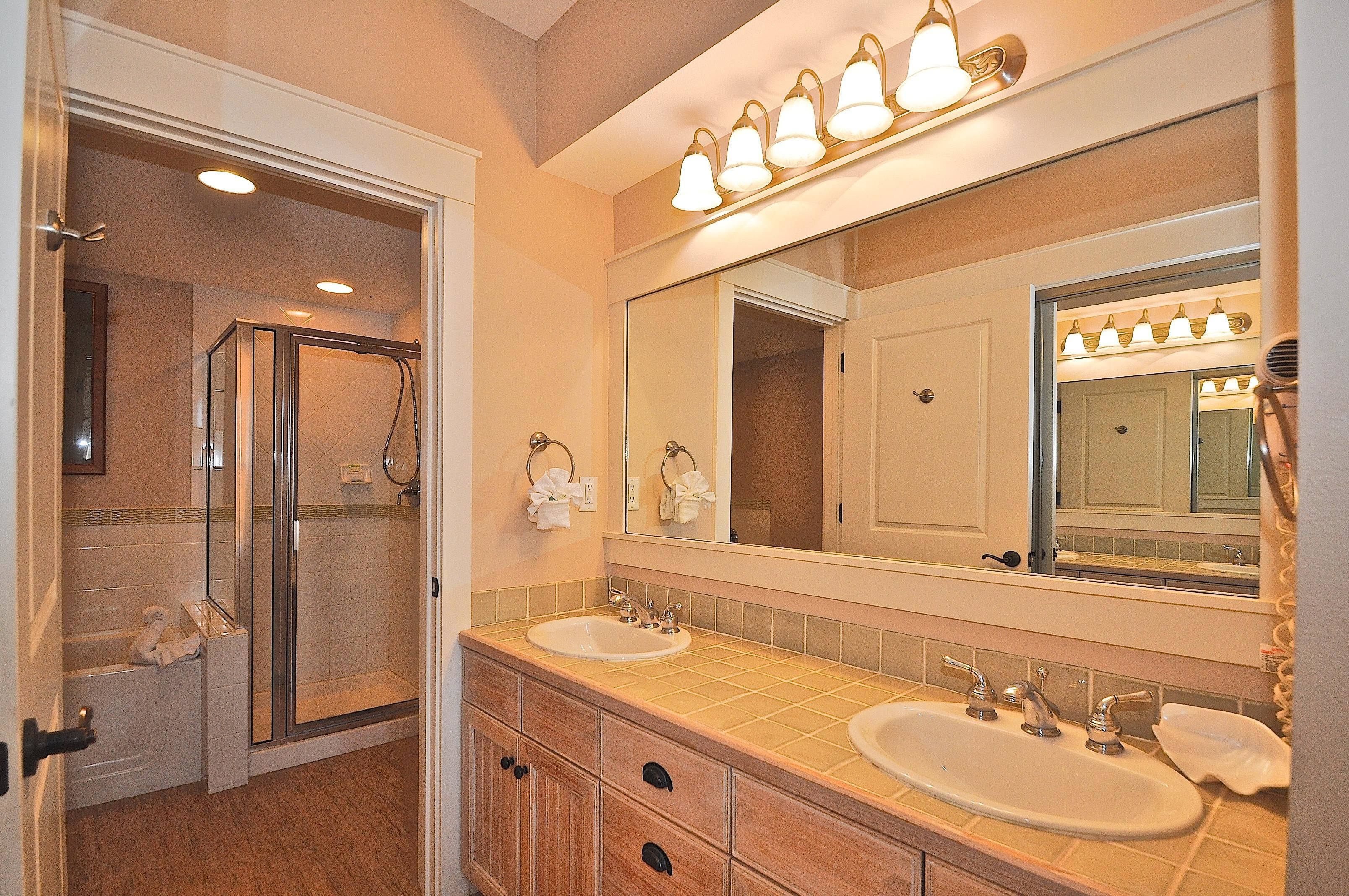 A bathroom with a walk-in shower, two sinks, a large mirror, and a towel rack.