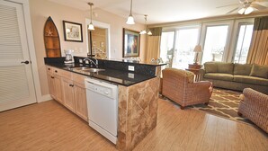 A kitchen with a dishwasher, a coffee maker, and a dining area with a sofa and chairs. - Observation Point 456 1 Bedroom Condo By Coastal Dreamin (Miramar Beach)