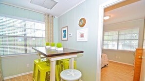 A dining area with a table and two yellow stools, a clock on the wall, and a window with blinds. - Grayton Beach Grayt Escape 2 Bedroom Holiday Home By Coastal Dreamin (Santa Rosa Beach)