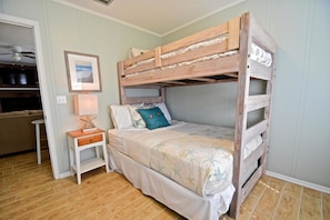 A bunk bed with a wooden frame, a bedside table with a lamp, and a framed picture on the wall.