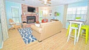 A living room with a beige sofa, a small table with yellow chairs, a brick fireplace, and a ceiling fan. - Grayton Beach Grayt Escape 2 Bedroom Holiday Home By Coastal Dreamin (Santa Rosa Beach)