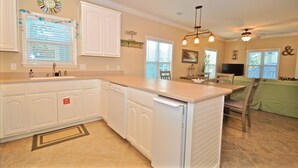 A kitchen with white cabinetry, a dishwasher, a sink, and a dining area with a table and chairs. - Old Florida Village Sea Psalm 4 Bedroom Holiday Home By Coastal Dreamin (Santa Rosa Beach)