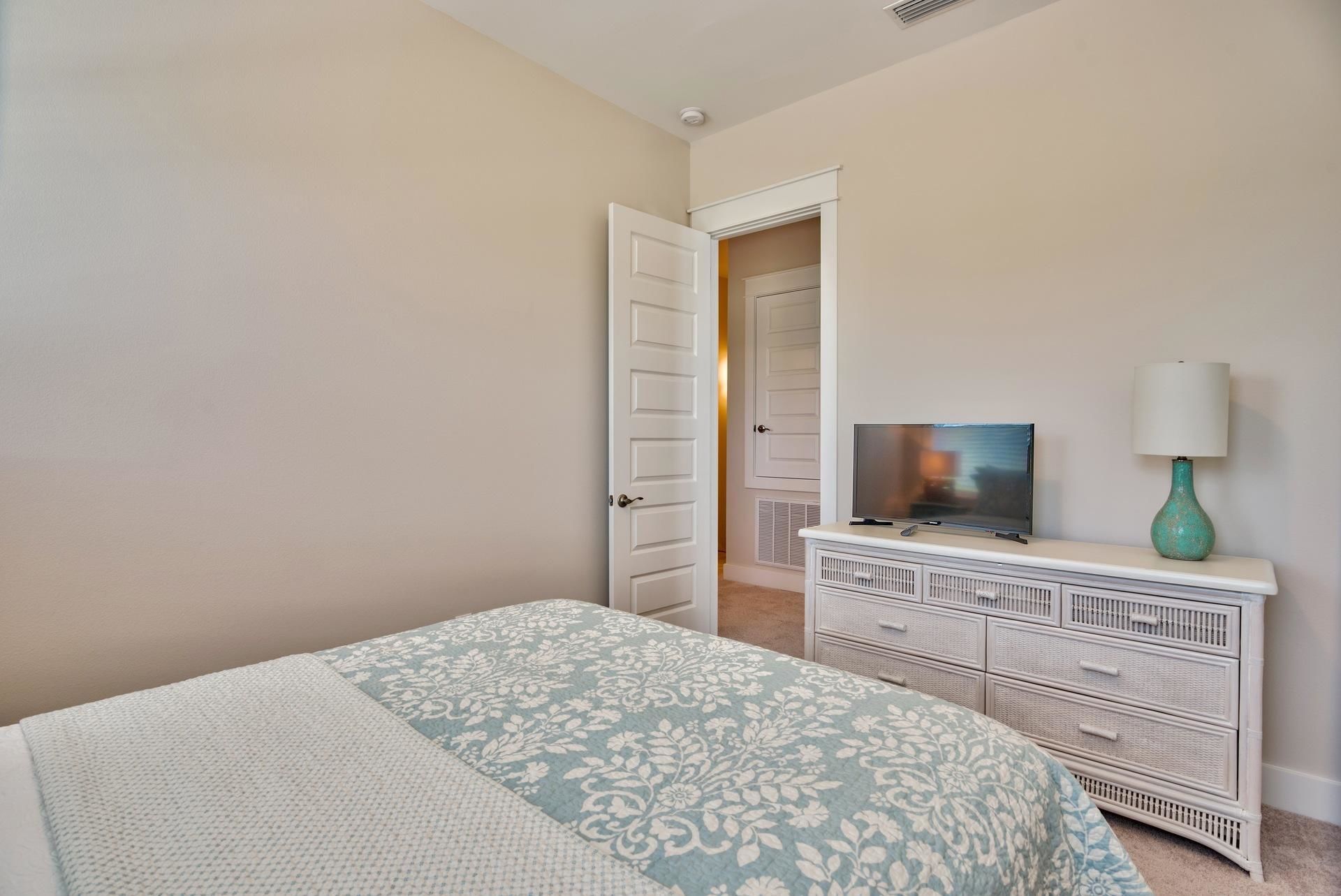 A bedroom with a bed, a dresser, a television, and a door leading to another room.