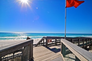 A wooden boardwalk leading to a beach with a lifeguard flag and a warning sign.