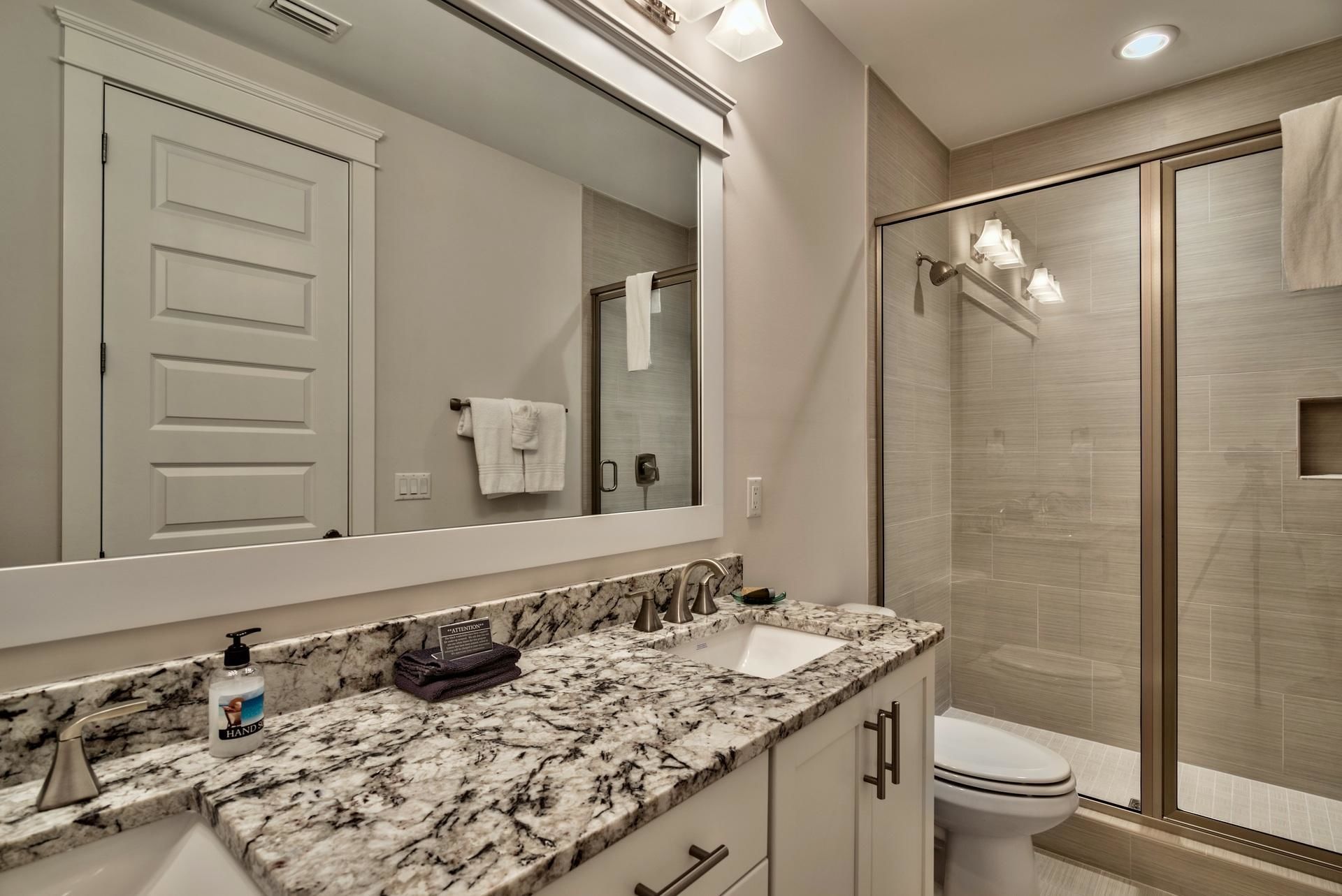 A modern bathroom with a marble countertop, a sink, a toilet, and a glass-enclosed shower.