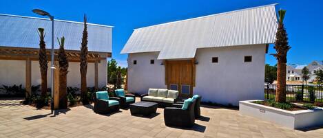 A patio area with outdoor furniture, a white building with a corrugated metal roof, and palm trees.