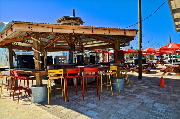 An outdoor seating area with a wooden pergola, red and yellow chairs, and a Coca-Cola branded umbrella.