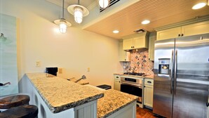 A kitchen with granite countertops, stainless steel appliances, and wooden bar stools. - Six Palms Dreamin 2 Bedroom Condo By Coastal Dreamin (Santa Rosa Beach)