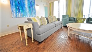 A living room with a gray sofa, a round coffee table, and a large abstract painting on the wall. - Six Palms Dreamin 2 Bedroom Condo By Coastal Dreamin (Santa Rosa Beach)
